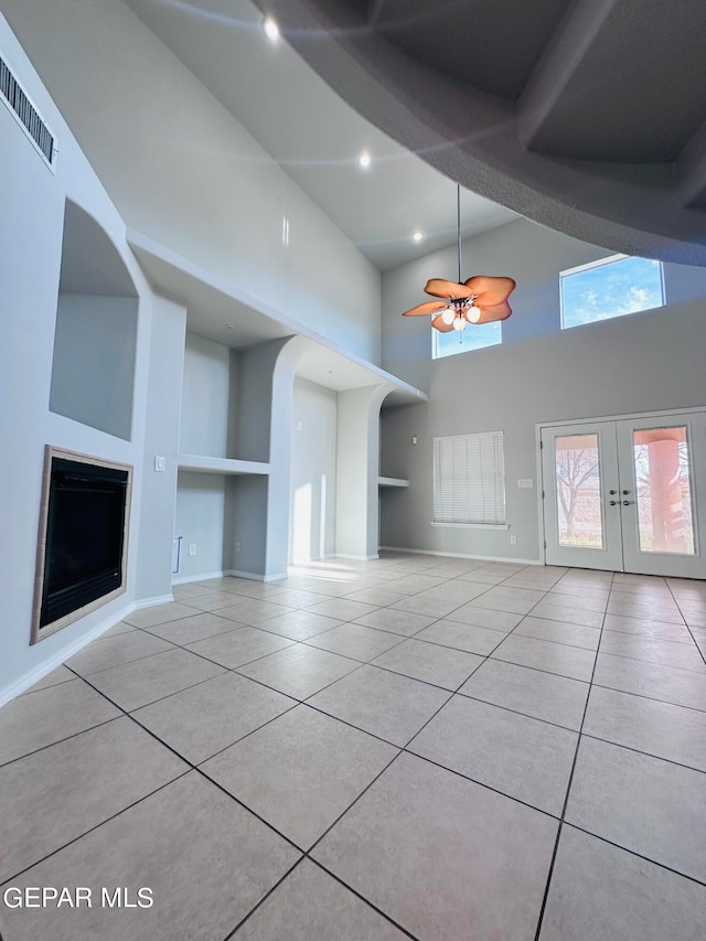 unfurnished living room featuring light tile floors, ceiling fan, french doors, a towering ceiling, and built in features