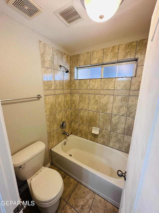 bathroom with tiled shower / bath, toilet, tile flooring, and a textured ceiling