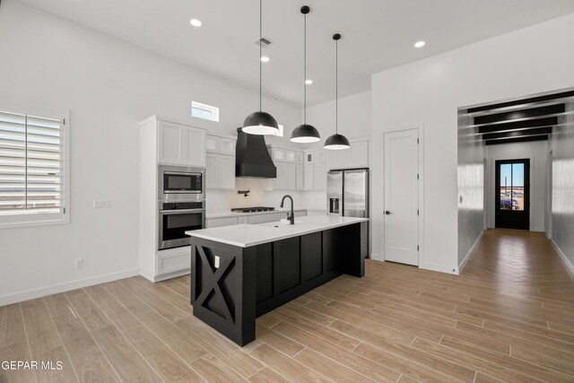 kitchen with white cabinets, hanging light fixtures, a kitchen island with sink, stainless steel appliances, and light countertops