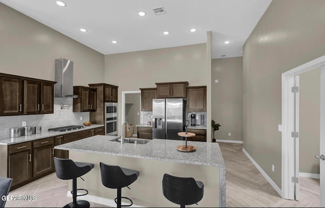 kitchen featuring stainless steel appliances, wall chimney range hood, light parquet floors, a breakfast bar area, and sink