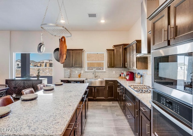 kitchen with appliances with stainless steel finishes, tasteful backsplash, light stone counters, sink, and a wealth of natural light