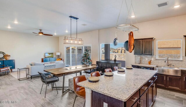 kitchen featuring a kitchen island, sink, light stone countertops, ceiling fan, and hanging light fixtures