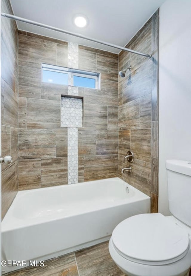 bathroom featuring tiled shower / bath combo, toilet, and tile flooring