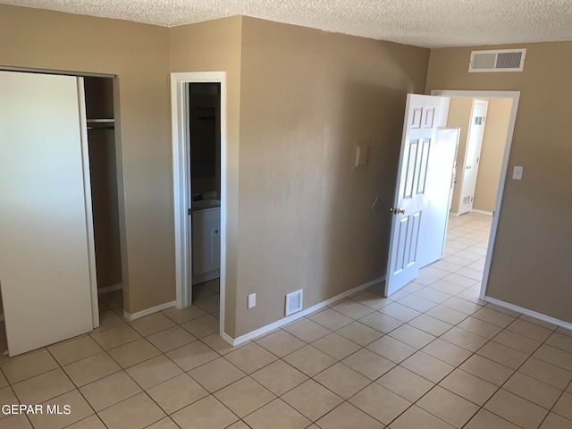 unfurnished bedroom with a textured ceiling, a closet, ensuite bathroom, and light tile floors