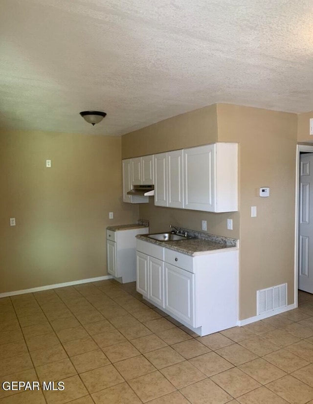 kitchen with light tile flooring, a textured ceiling, white cabinetry, and sink