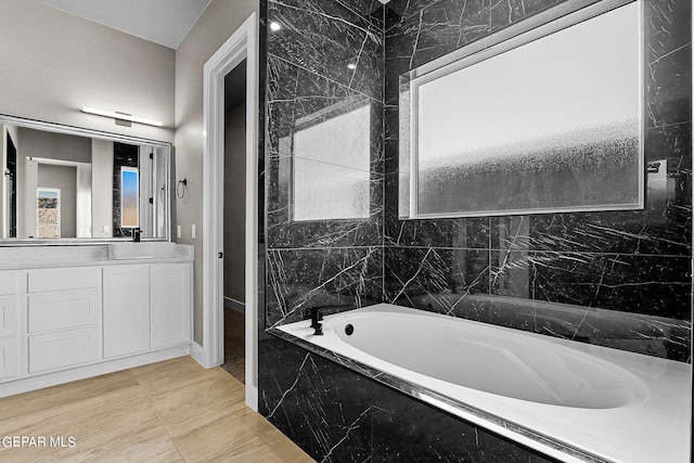 bathroom with plenty of natural light, a relaxing tiled tub, and vanity