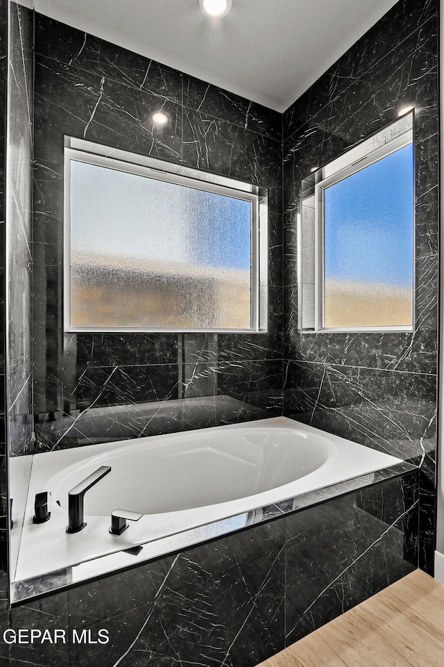 bathroom with tiled tub and tile walls