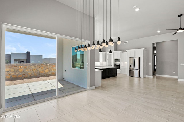 interior space with a kitchen island with sink, ceiling fan, stainless steel appliances, hanging light fixtures, and white cabinetry