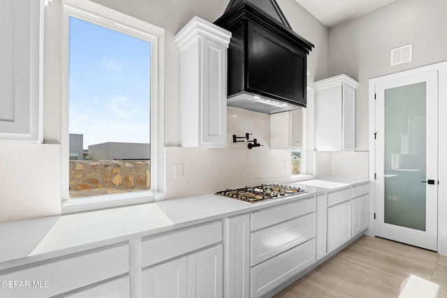 kitchen with custom exhaust hood, light hardwood / wood-style floors, white cabinetry, and stainless steel gas cooktop