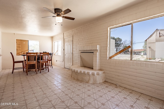 dining area featuring brick wall, a textured ceiling, ceiling fan, and light tile flooring