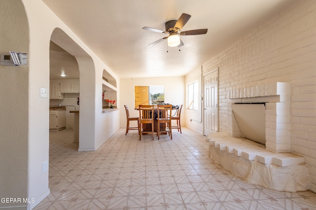 dining room featuring ceiling fan, brick wall, and light tile floors