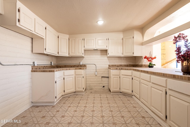 kitchen with white cabinets, brick wall, light tile flooring, and tile counters