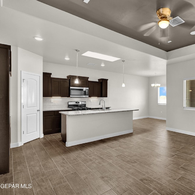 kitchen featuring appliances with stainless steel finishes, pendant lighting, tasteful backsplash, ceiling fan with notable chandelier, and a center island with sink