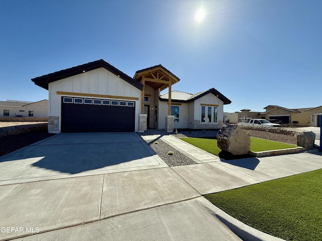 view of front of home featuring driveway, a front lawn, stone siding, board and batten siding, and an attached garage