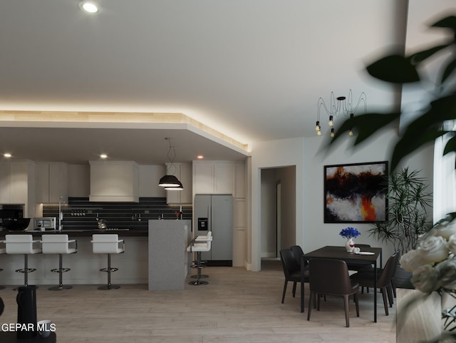 kitchen with a kitchen breakfast bar, stainless steel refrigerator with ice dispenser, tasteful backsplash, wall chimney exhaust hood, and light wood-type flooring