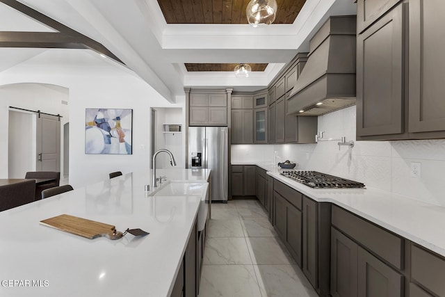 kitchen featuring backsplash, custom exhaust hood, stainless steel appliances, a tray ceiling, and a barn door