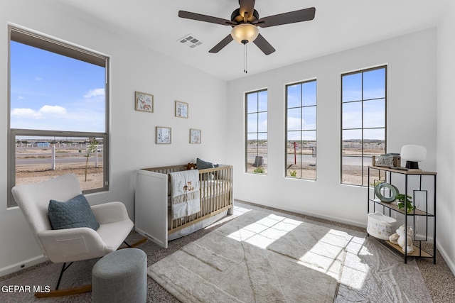 carpeted bedroom with ceiling fan and a crib