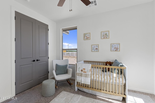 carpeted bedroom with a crib, a closet, and ceiling fan