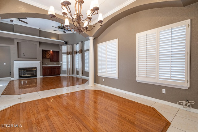 unfurnished living room with ceiling fan with notable chandelier, crown molding, a tile fireplace, light tile patterned floors, and plenty of natural light