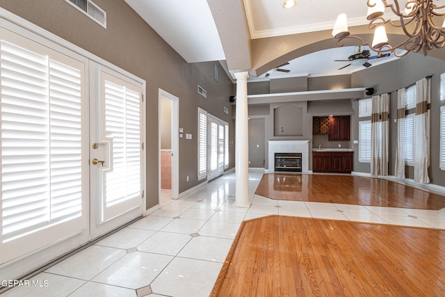 unfurnished living room featuring ceiling fan with notable chandelier, light tile patterned floors, crown molding, and ornate columns