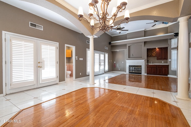 unfurnished living room featuring a tile fireplace, french doors, ceiling fan with notable chandelier, crown molding, and light tile patterned floors