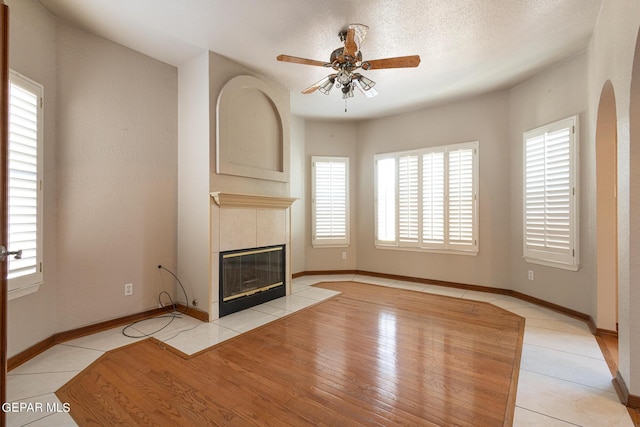 18 Via Placita, El Paso, TX 79927 - unfurnished living room featuring a tiled fireplace, ceiling fan, baseboards, arched walkways, and tile patterned floors