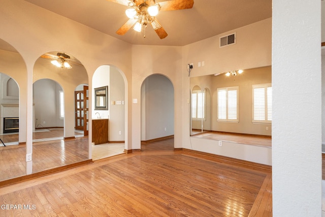 18 Via Placita, El Paso, TX 79927 - unfurnished living room featuring ceiling fan, wood finished floors, a tiled fireplace, baseboards, and arched walkways