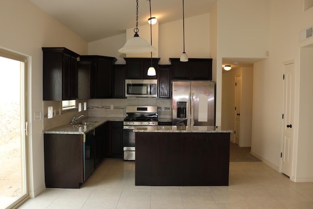 kitchen with appliances with stainless steel finishes, a center island, light tile floors, hanging light fixtures, and light stone countertops