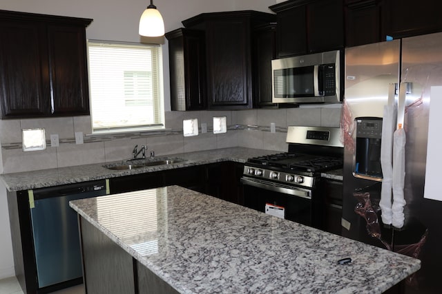 kitchen with light stone countertops, decorative light fixtures, appliances with stainless steel finishes, tasteful backsplash, and sink