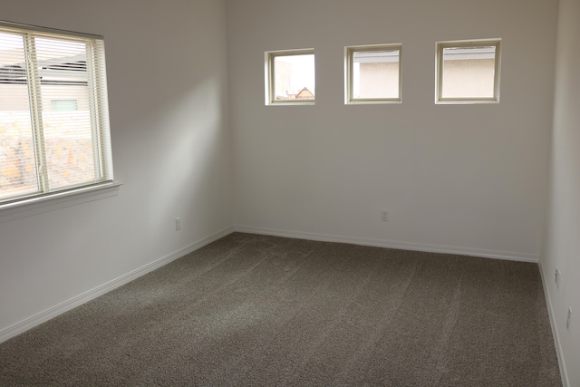 unfurnished room with dark colored carpet and plenty of natural light