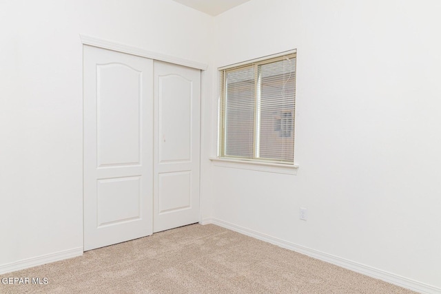 unfurnished bedroom with light colored carpet and a closet