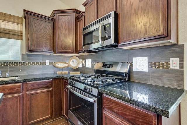 kitchen featuring sink, backsplash, stainless steel appliances, and dark stone counters