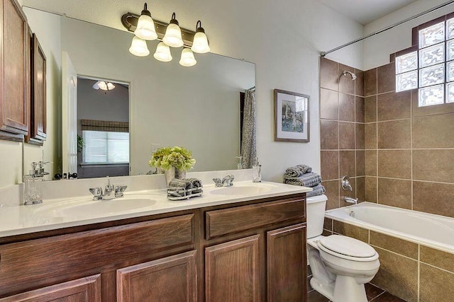 full bathroom with tile flooring, tiled shower / bath, vanity with extensive cabinet space, double sink, and toilet