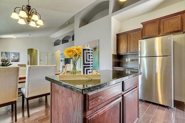 kitchen with an inviting chandelier, appliances with stainless steel finishes, a kitchen island, tasteful backsplash, and dark stone counters