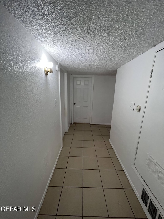 hall with a textured ceiling and light tile flooring