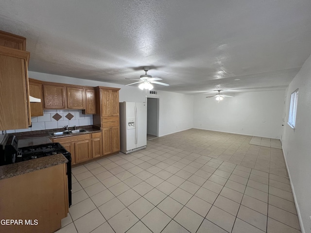 kitchen with backsplash, ceiling fan, white fridge with ice dispenser, black range oven, and sink