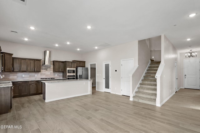 kitchen with stainless steel appliances, light hardwood / wood-style floors, a center island with sink, tasteful backsplash, and wall chimney range hood