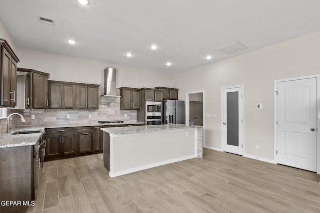 kitchen with wall chimney exhaust hood, a center island, light stone countertops, stainless steel appliances, and tasteful backsplash