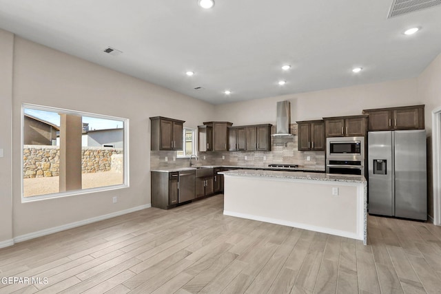 kitchen with wall chimney exhaust hood, appliances with stainless steel finishes, light hardwood / wood-style flooring, and a center island