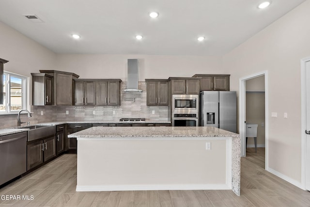 kitchen featuring appliances with stainless steel finishes, a center island, wall chimney range hood, and light stone counters