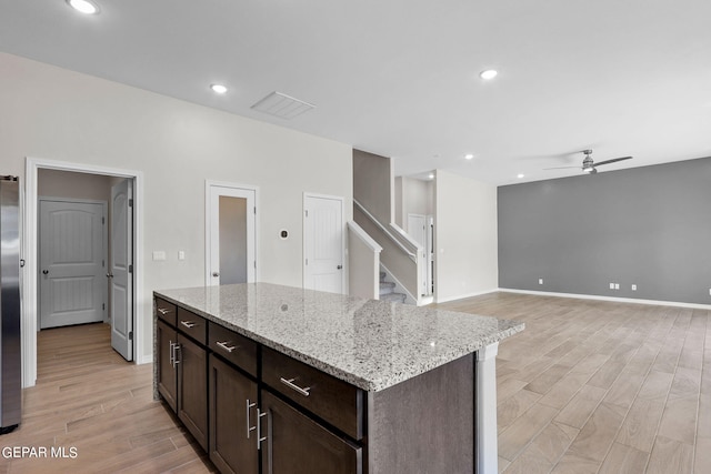 kitchen featuring light stone counters, ceiling fan, a kitchen island, dark brown cabinets, and light hardwood / wood-style flooring