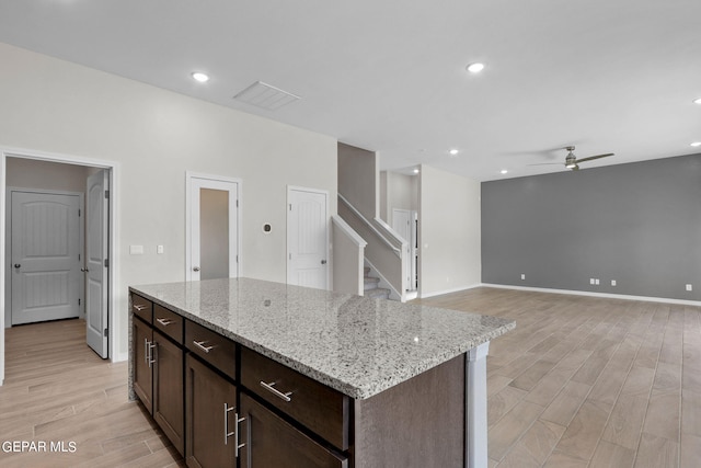 kitchen featuring light stone countertops, dark brown cabinetry, light wood-type flooring, a kitchen island, and ceiling fan