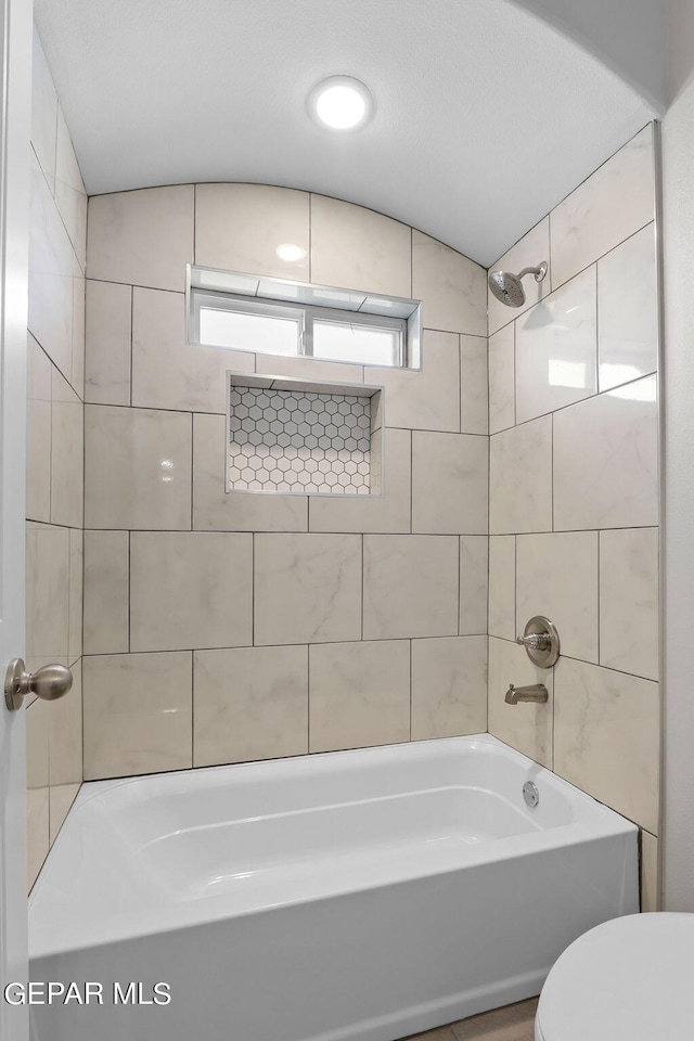 bathroom featuring tiled shower / bath combo and toilet