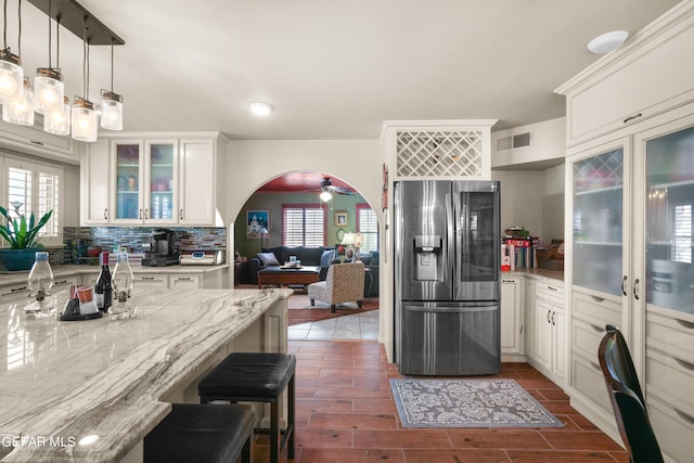 kitchen featuring hanging light fixtures, stainless steel refrigerator with ice dispenser, white cabinetry, a kitchen bar, and tasteful backsplash