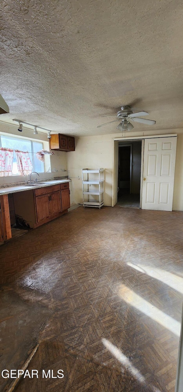 kitchen with ceiling fan, light countertops, brown cabinetry, a textured ceiling, and a sink