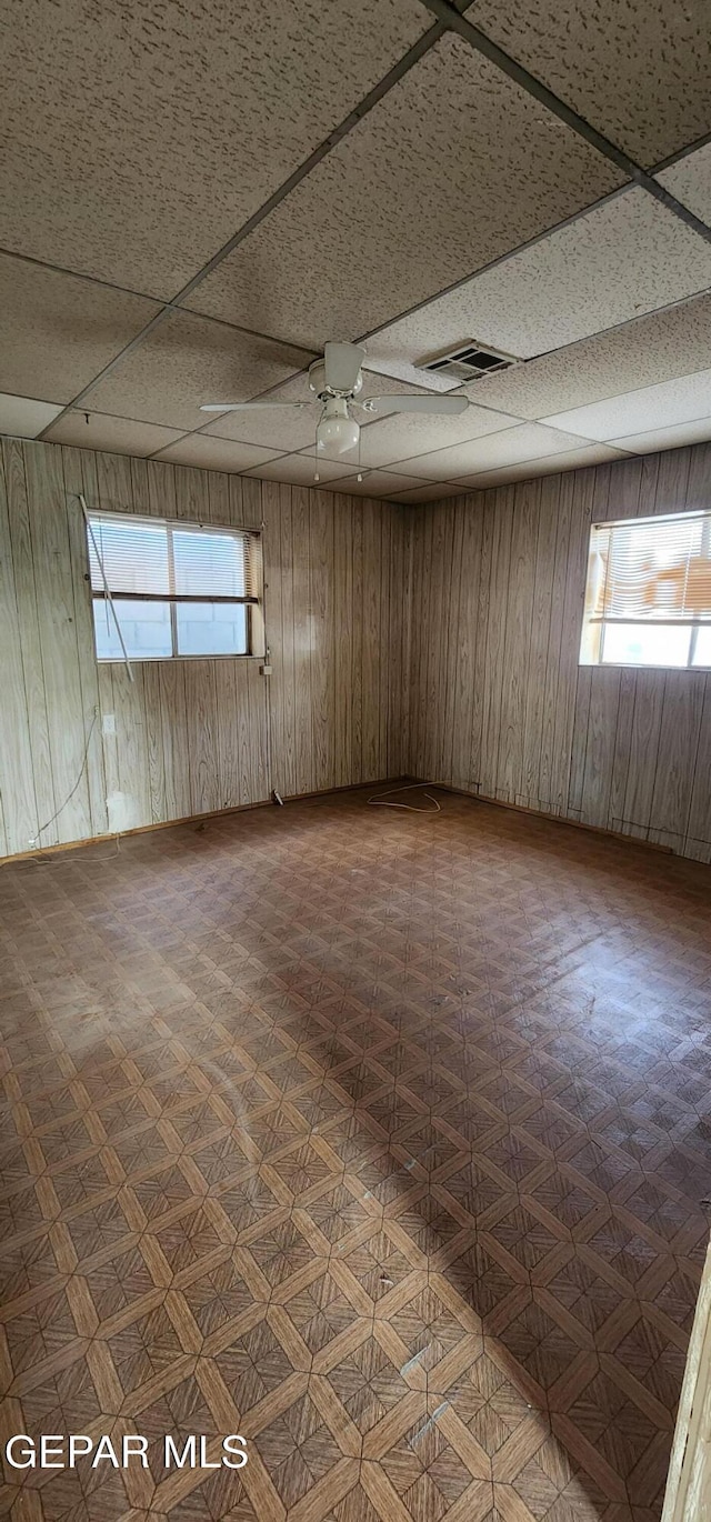 unfurnished room with a paneled ceiling, visible vents, wood walls, and ceiling fan