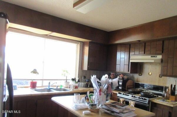 kitchen featuring dark brown cabinets, sink, gas range oven, and stainless steel fridge