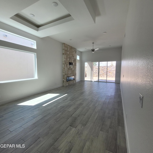 unfurnished living room with plenty of natural light, a fireplace, dark wood-type flooring, and ceiling fan