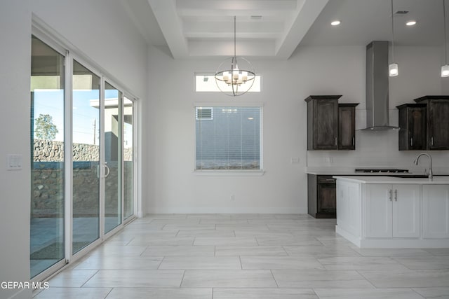 kitchen with a raised ceiling, hanging light fixtures, wall chimney exhaust hood, a notable chandelier, and dark brown cabinetry