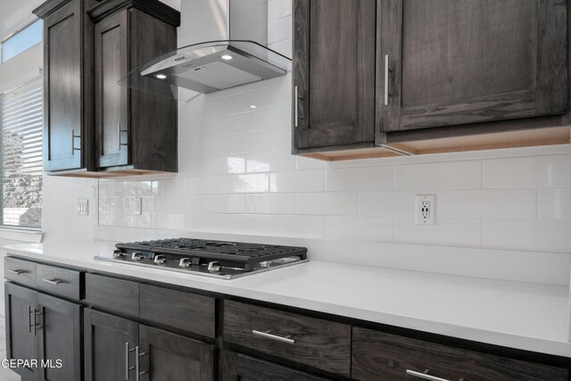 kitchen featuring backsplash, dark brown cabinets, wall chimney exhaust hood, and stainless steel gas stovetop